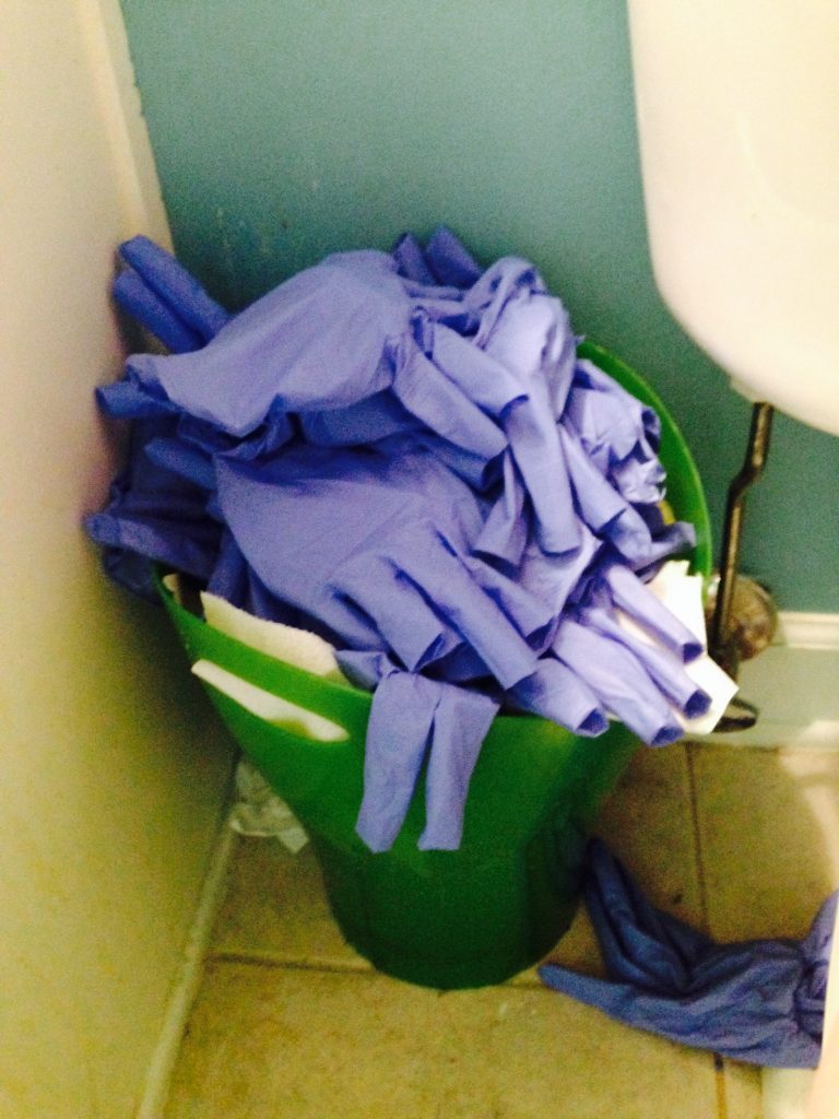 bathroom bin filled with pairs of blue gloves from a single day