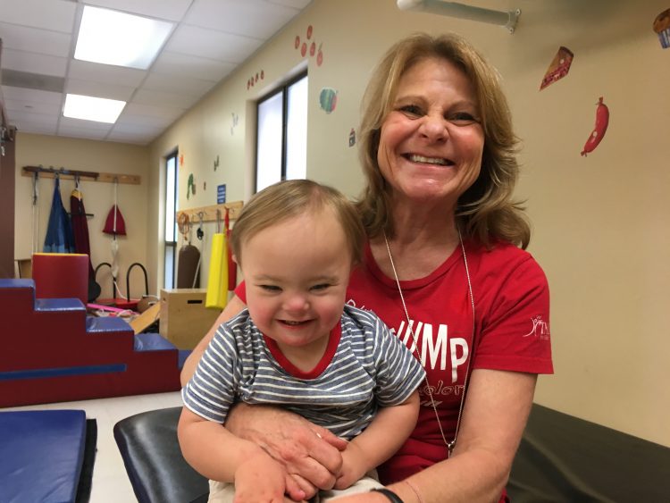 A little boy with Down syndrome sitting on his therapist's lap for a photo