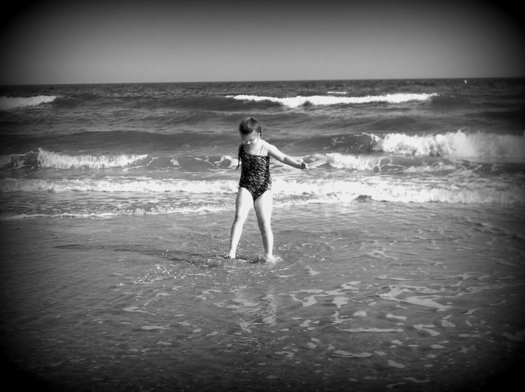 black and white photo of young girl walking along the beach