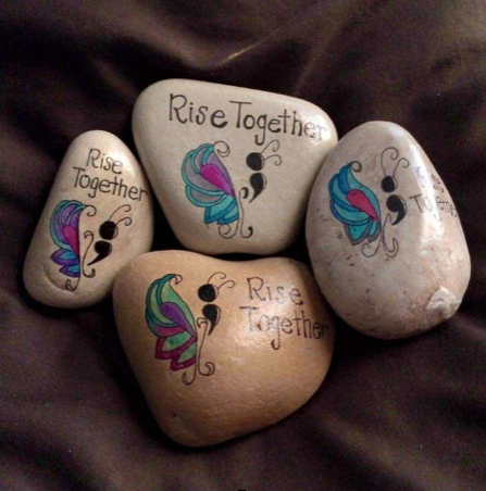Rocks with butterflied painted on them that say "Rise Together"