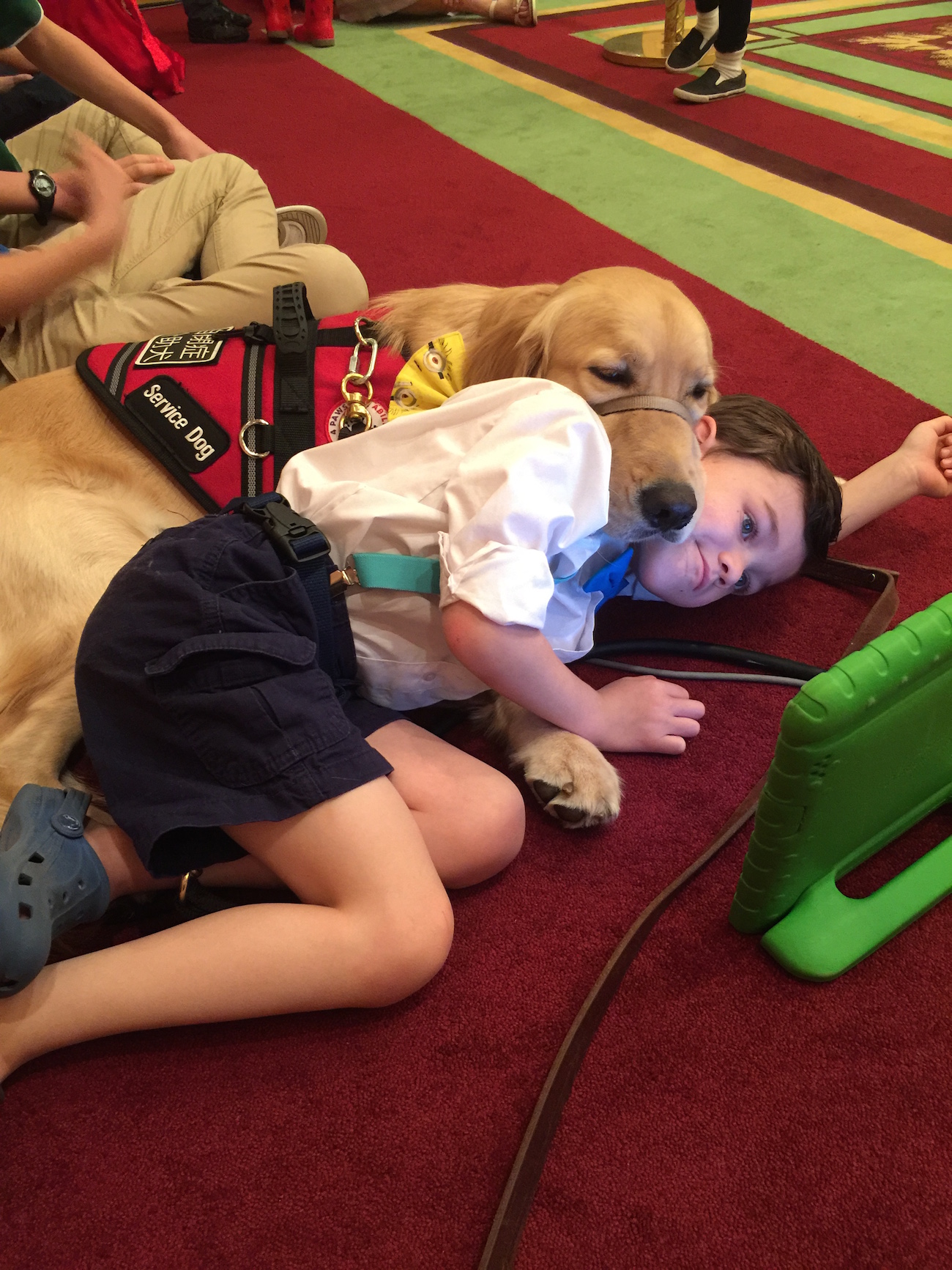 The author's son Kai and Tornado his service dog lying on the carpeted floor, watching an iPad