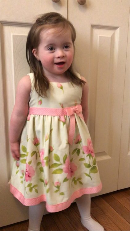 Little girl with Down syndrome standing in front of a white door wearing an Easter dress