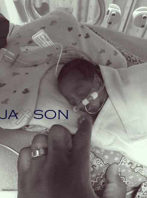 A black and white photo of baby Jaxson in the NICU with his hand around his parent's finger