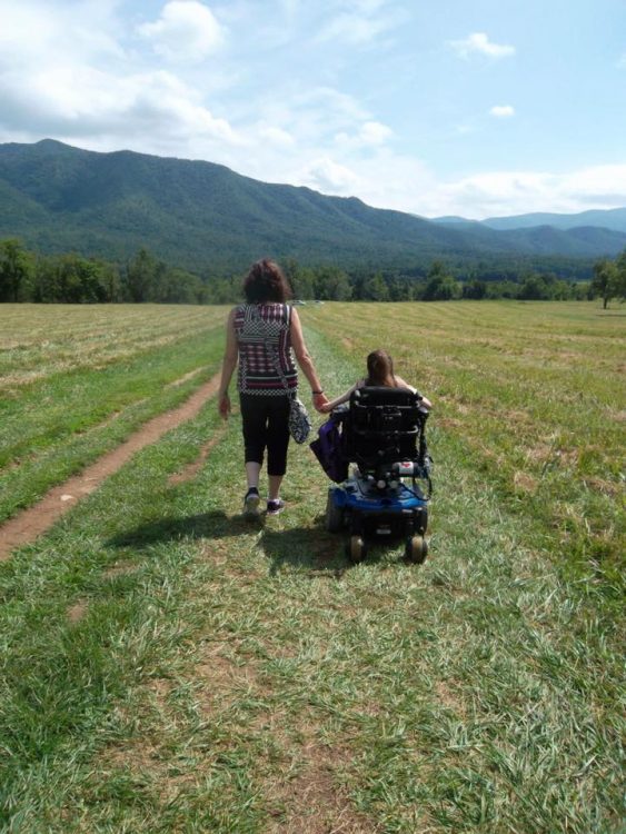 woman in wheelchair holding hands with mom, facing mountain
