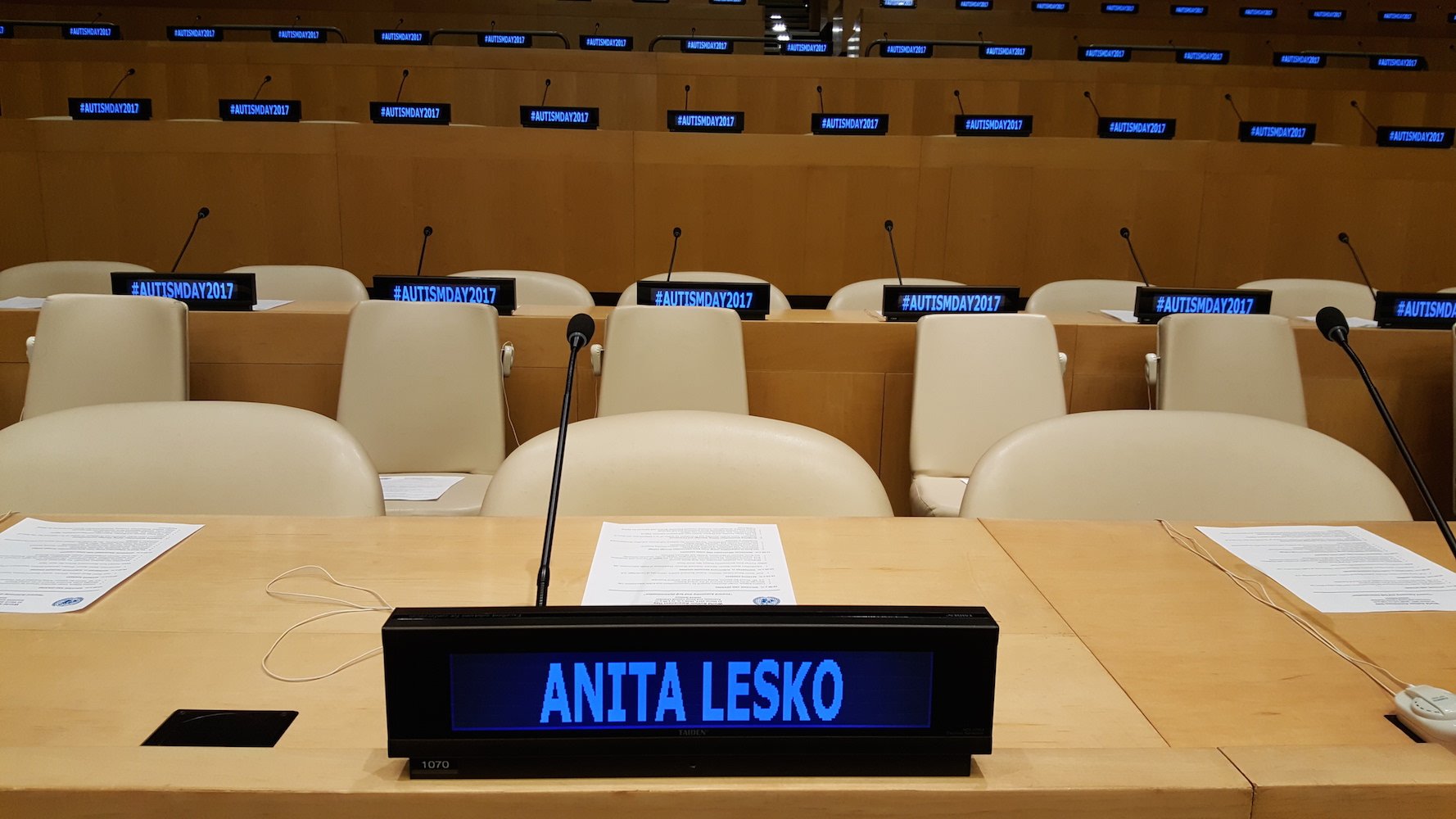 UN tables and chairs with a digital nameplate reading Anita Lesko and digital name plates on tables in the background that say Autism Day 2017