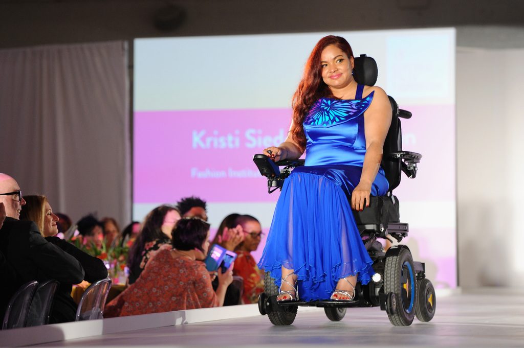 A model in blue dress using a power wheelchair.
