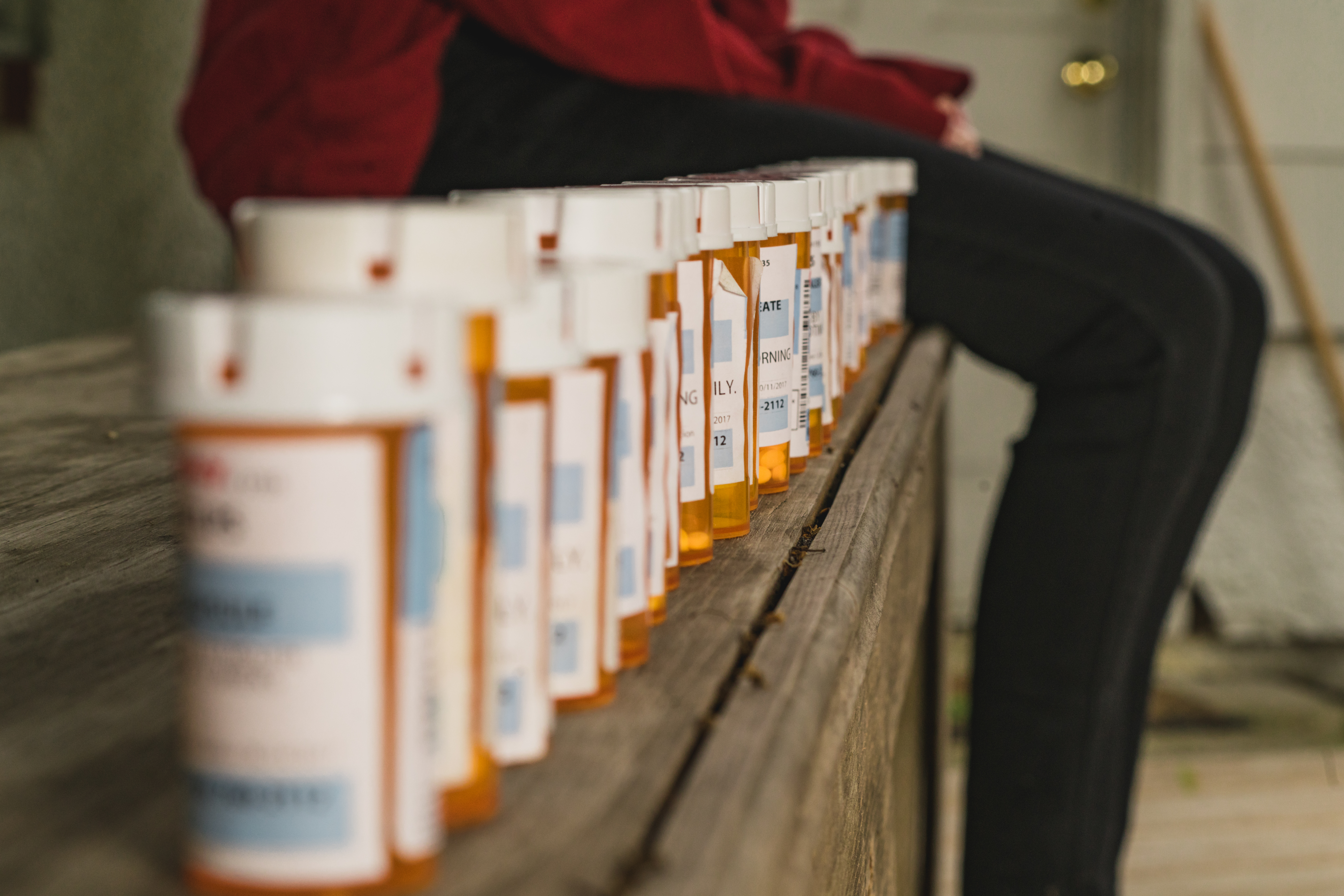 woman on bench with 20 medication bottles