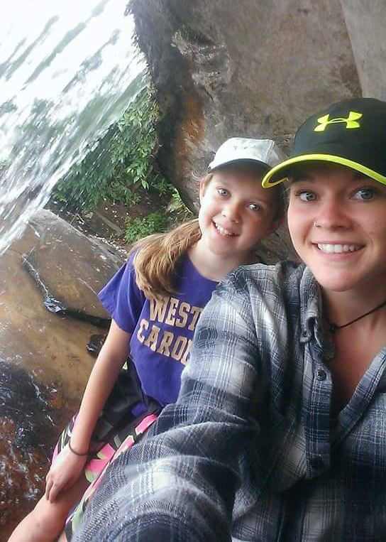 young woman and little sister smiling on rocks behind waterfall