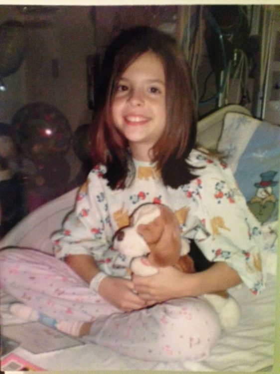 young girl sitting in a hospital bed with a stuffed animal