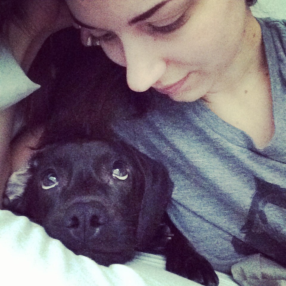 image of young woman looking down at black labrador dog