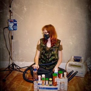 woman sitting on the floor with a mask over her mouth and pill bottles in front of her
