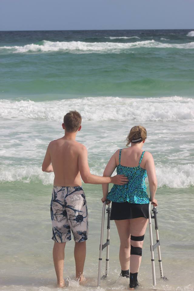 The author with her walker and her son next to her, both walking on beach toward water
