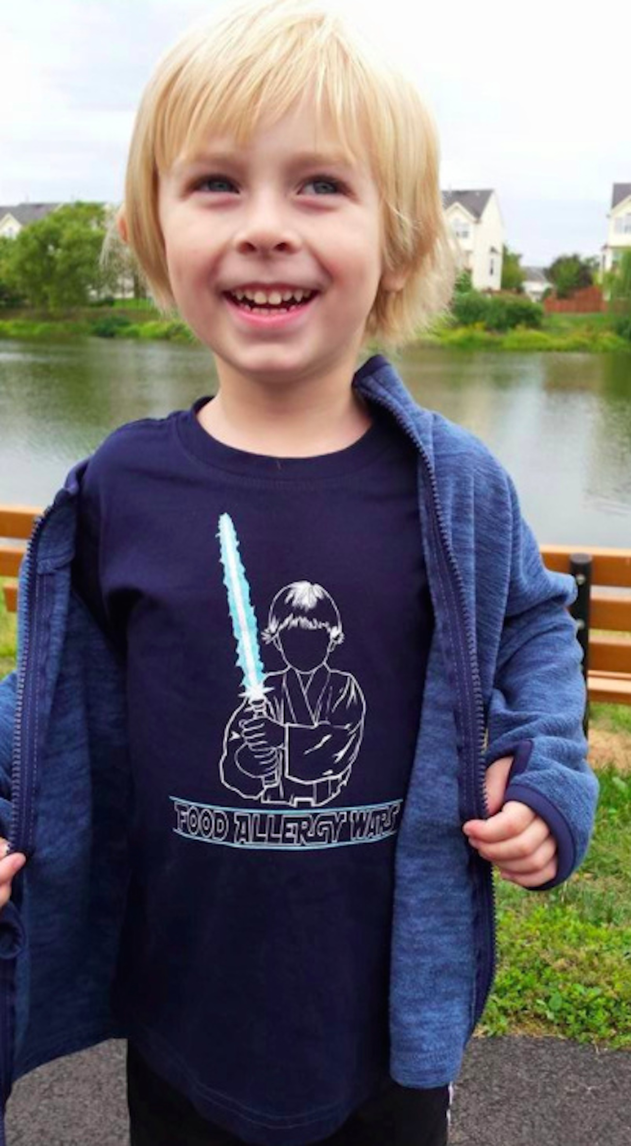 Boy wearing a jacket over a t-shirt that says food allergy wars and has an illustration of a boy holding a lightsaber