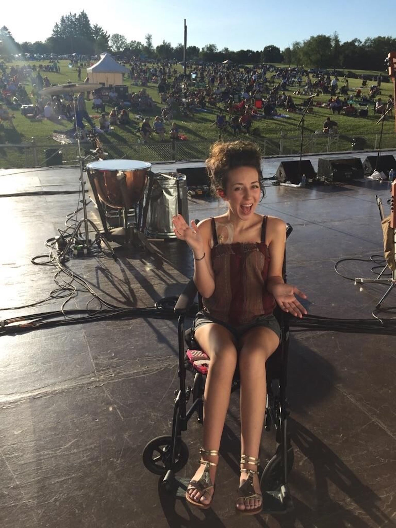 young woman sitting in a wheelchair on a stage looking over crowd of people