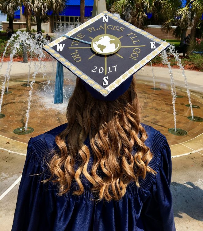 college graduate standing in front of a fountain wearing her cap and gown