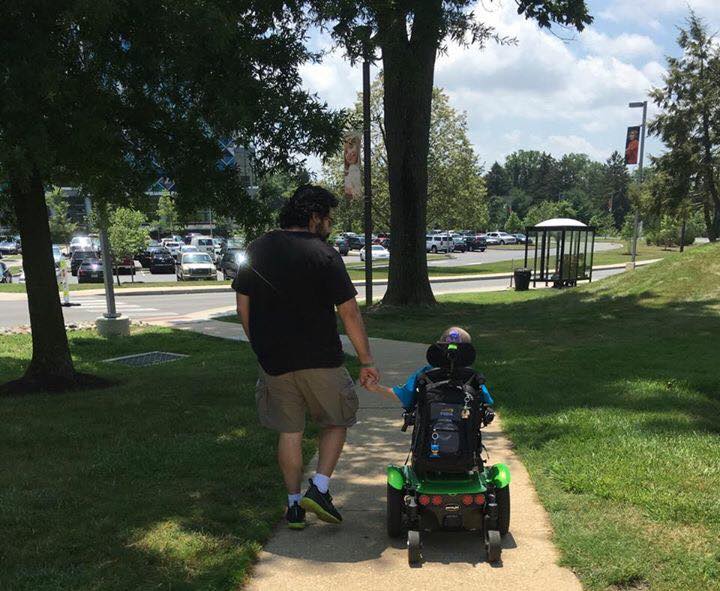 dad holding the hand of his son who is in a wheelchair