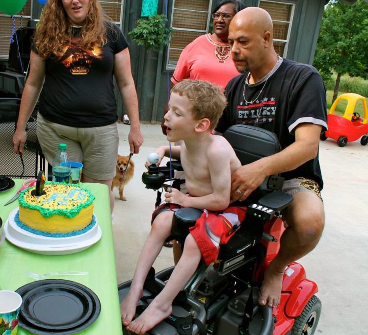 dad helping son in wheelchair blow out candles on his birthday cake