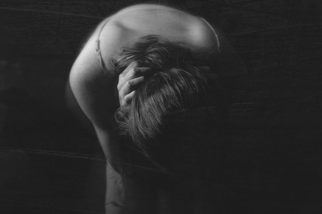 Black and white image of photographer's representation of how depression affects her body, woman arched over with hands behind neck showing back
