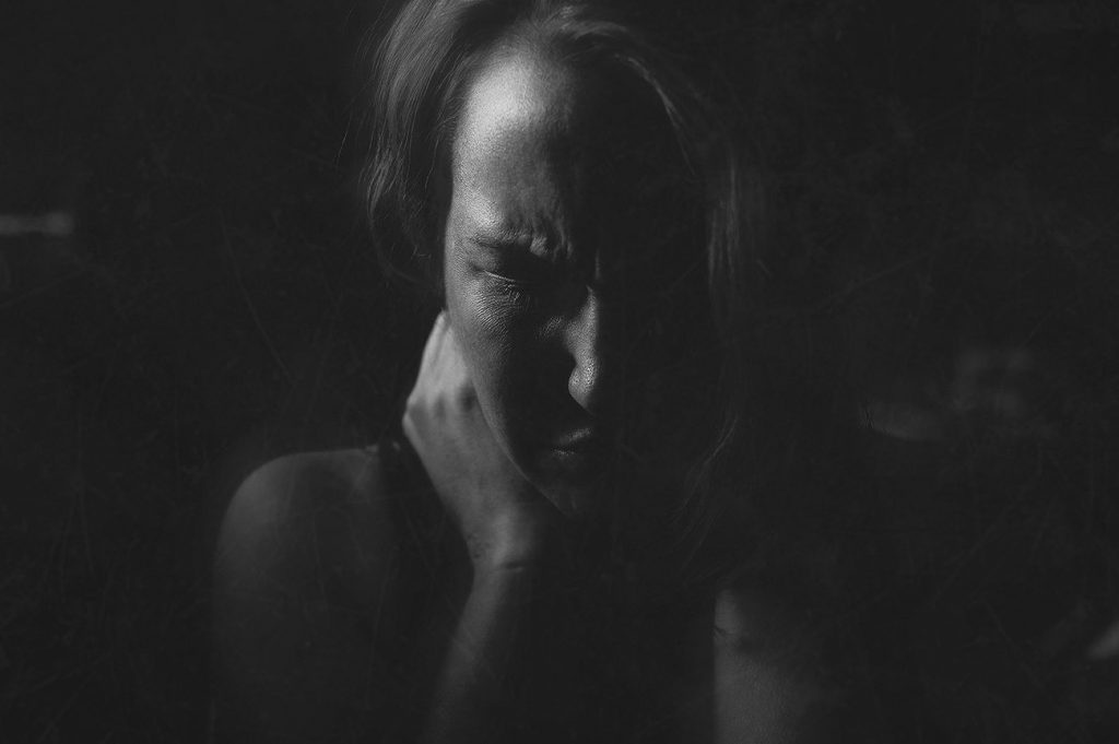 Black and white image of photographer's representation of how depression affects her mind hands behind head grimaced in pain