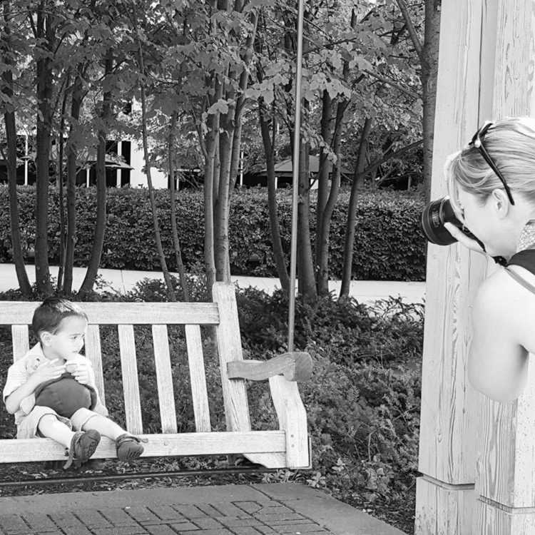 Black and white photo of photographer taking picture of a child with autism sitting on a swing bench