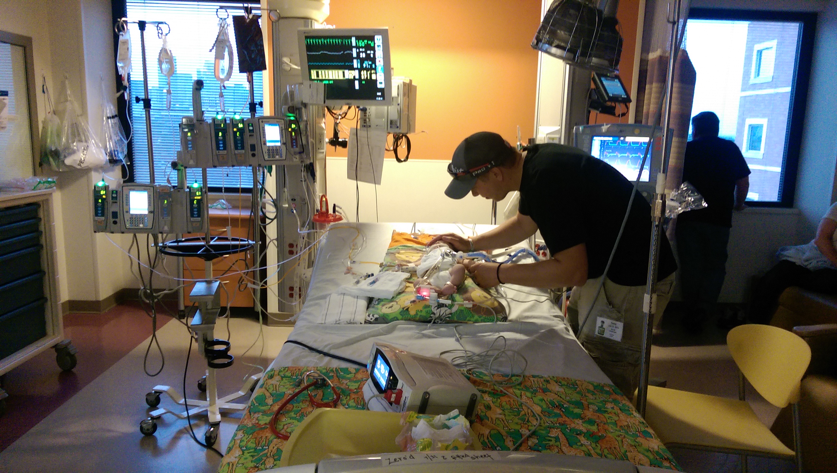 The author next to his baby who is lying in a hospital bed