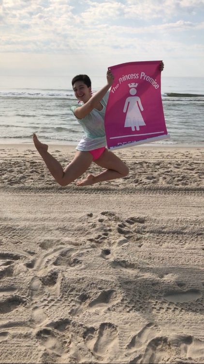 woman jumping on the beach with her princess promise sign