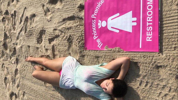 woman lying on the beach next to her princess promise sign