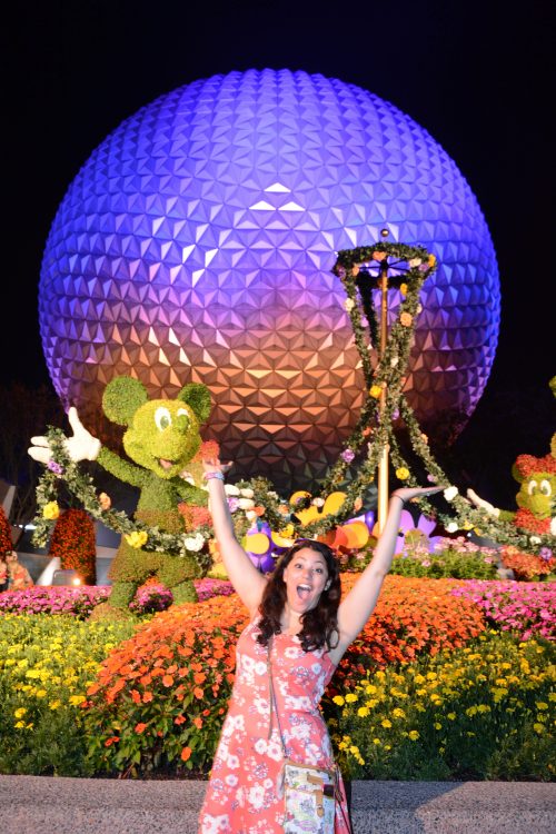 woman smiling and waving her arms in front of epcot at disney