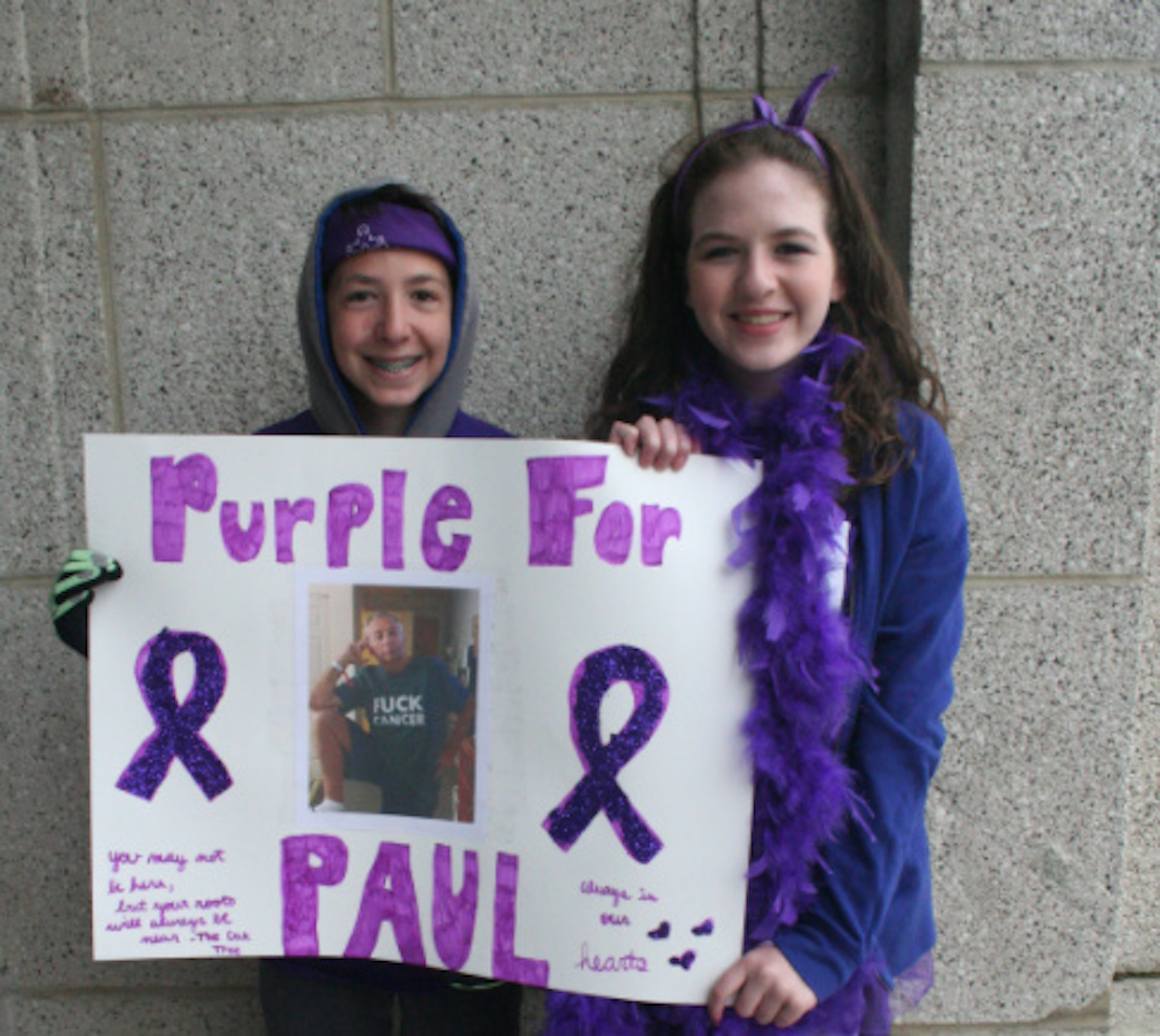 Two people holding a handmade sign that says "Purple for Paul" with a photo and purple ribbons