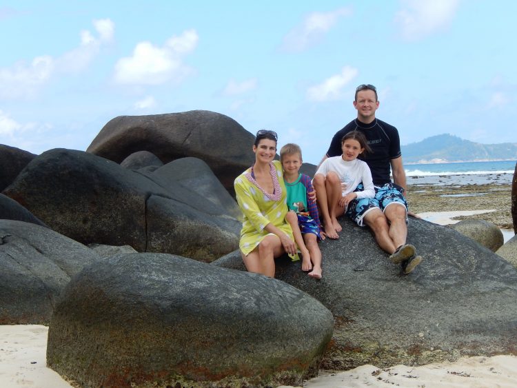 family sitting on a big rock on a beach