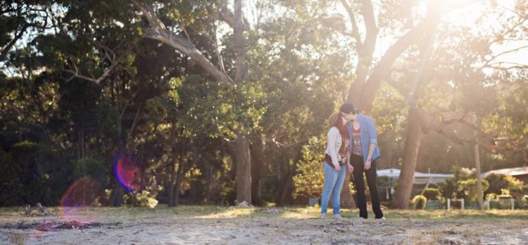 couple kissing outside in front of trees