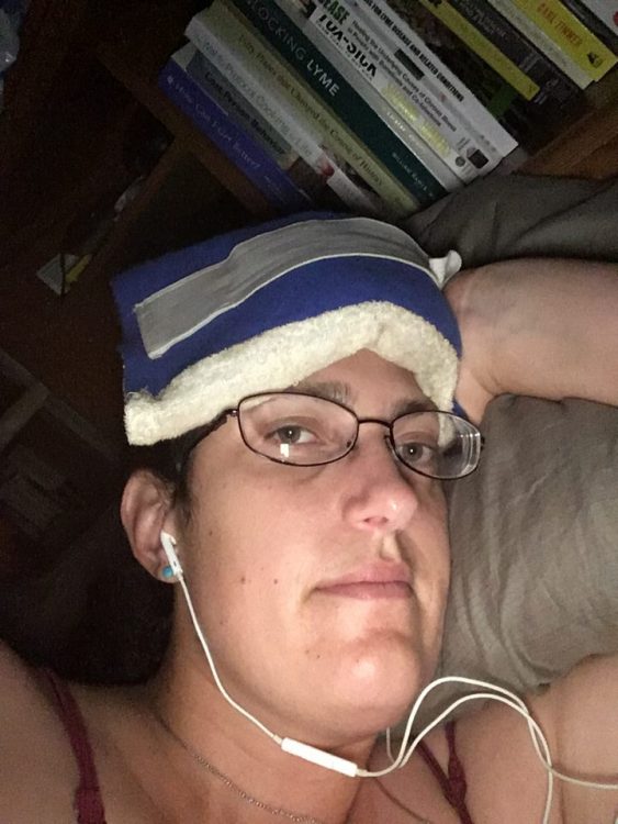 woman in bed with an ice pack on her head and earphones in