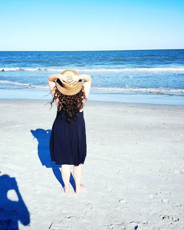 woman standing on the beach in a black sundress and hat