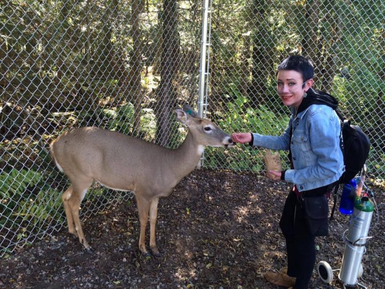 A young woman with oxygen feeds a deer.