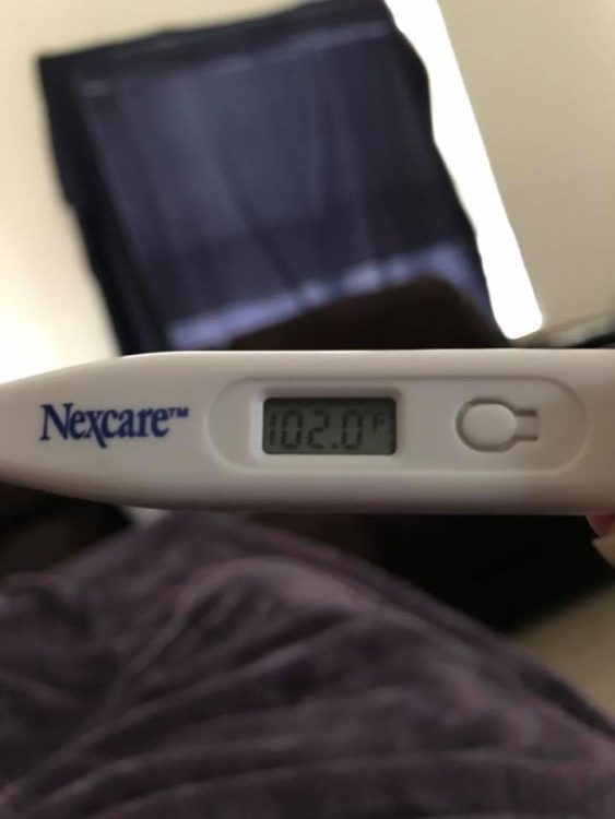 woman lying in bed holding up a thermometer that reads 102 degrees fahrenheit