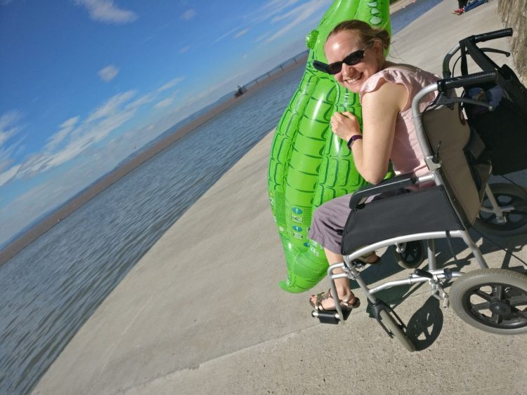 woman sitting in her wheelchair holding a pool float next to a lake