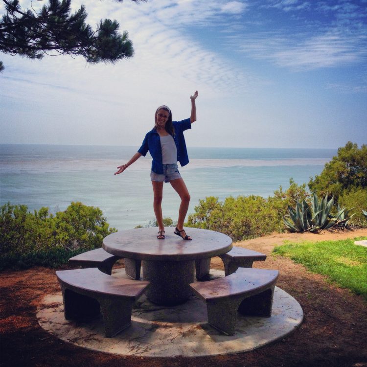 woman standing on table that overlooks the ocean