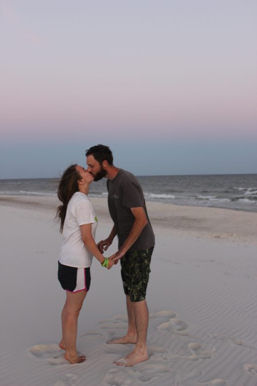 wife and husband kissing on the beach at sunset