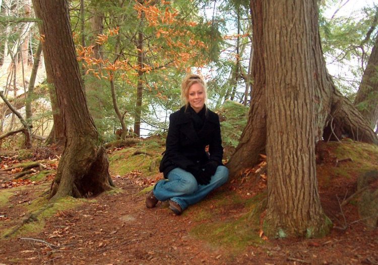 woman sitting in the forest next to a tree