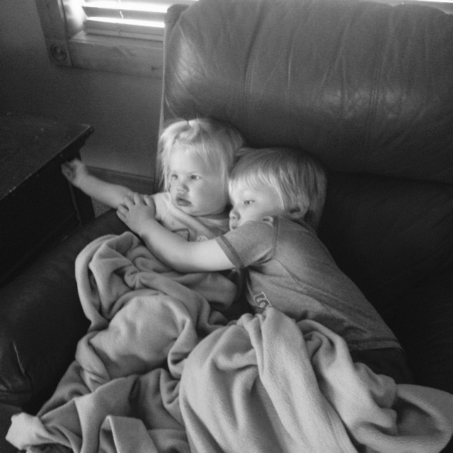 toddler boy and girl sitting on a couch under blankets hugging