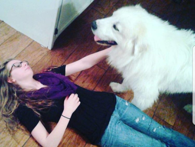 woman lying on the floor petting a big white dog