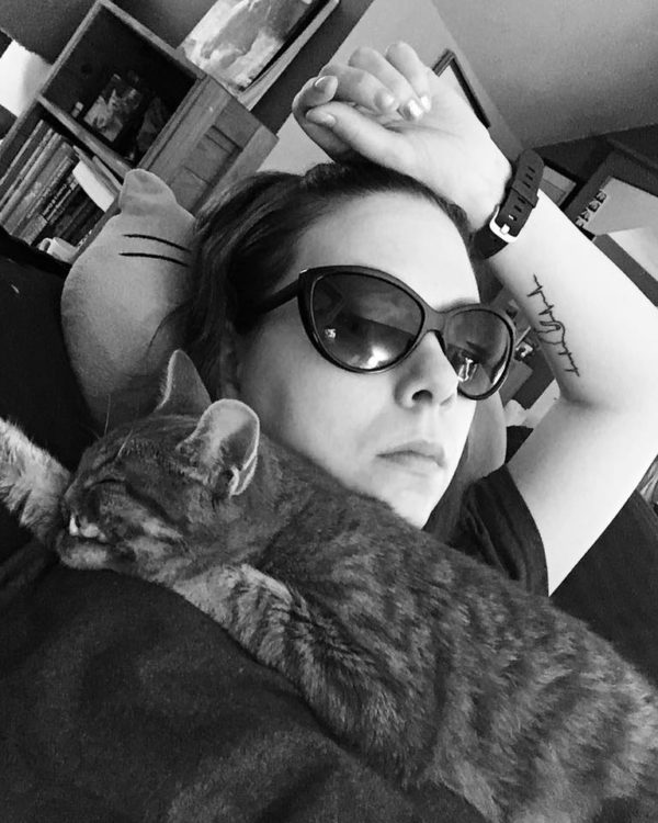black and white photo of woman lying on couch wearing sunglasses and holding her cat