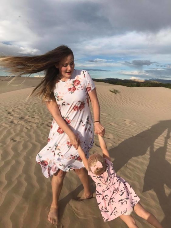 woman holding her daughter's hands and twirling her around on the beach