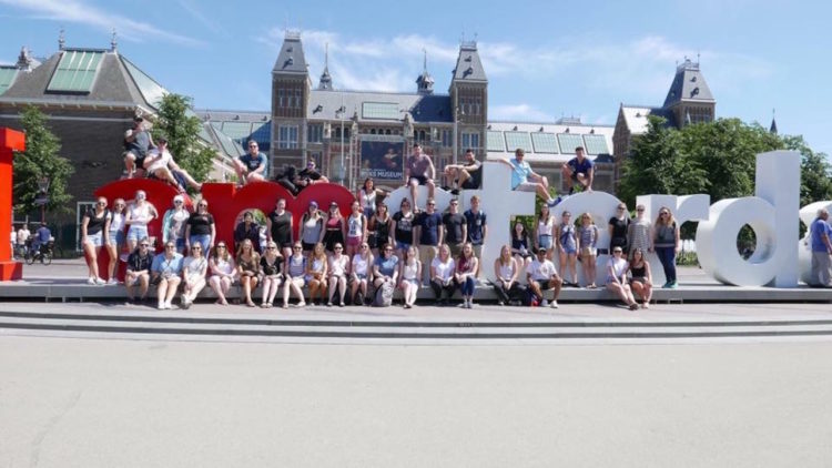 group sitting in front of the 'I amsterdam" sign