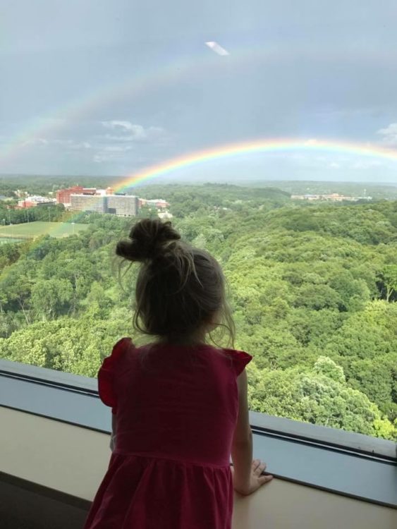 girl looking out the window at a rainbow