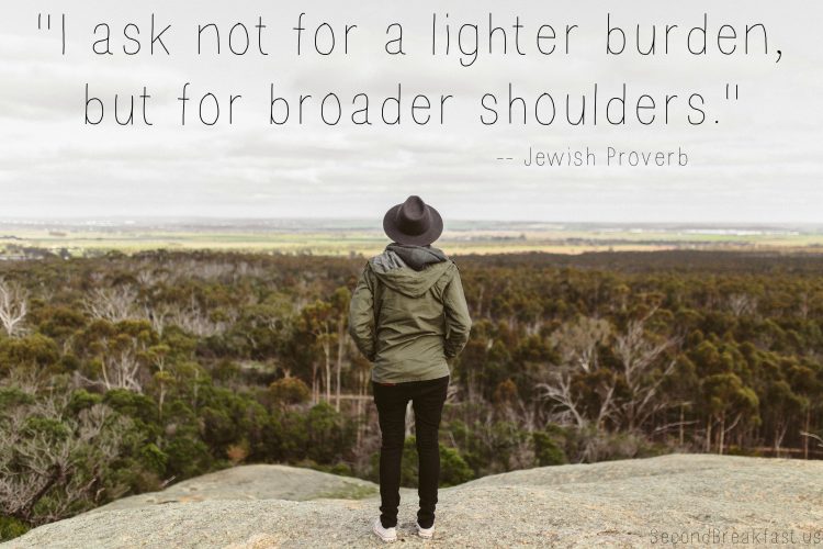 woman standing on hill overlooking landscape with the text "I ask not for a lighter burden, but for bigger shoulders."