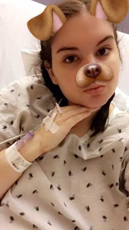 A girl in a hospital gown and bed, with a dog Snapchat filter on her face.