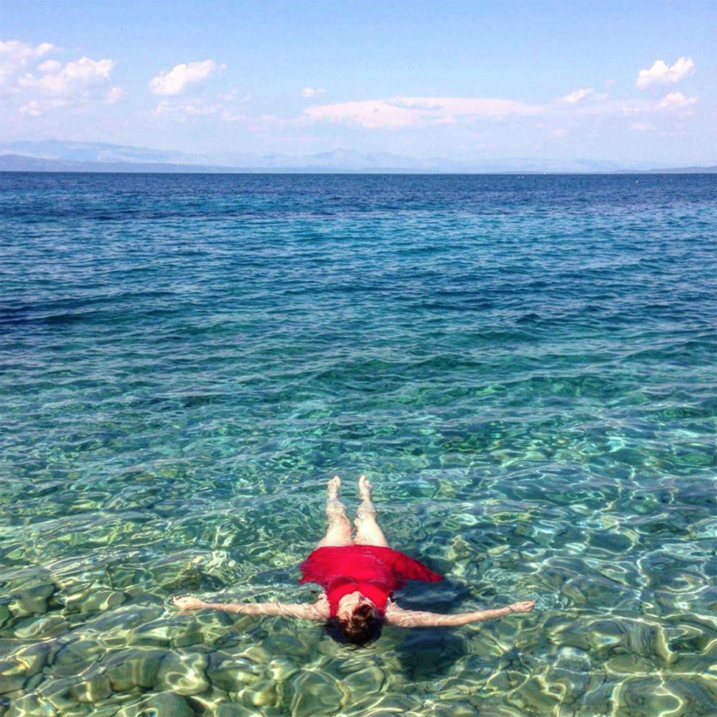 young woman lying in clear ocean wearing red bathing suit