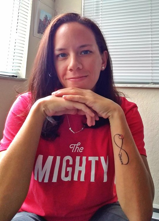 woman smiling and wearing 'the mighty' shirt with a tattoo on her arm