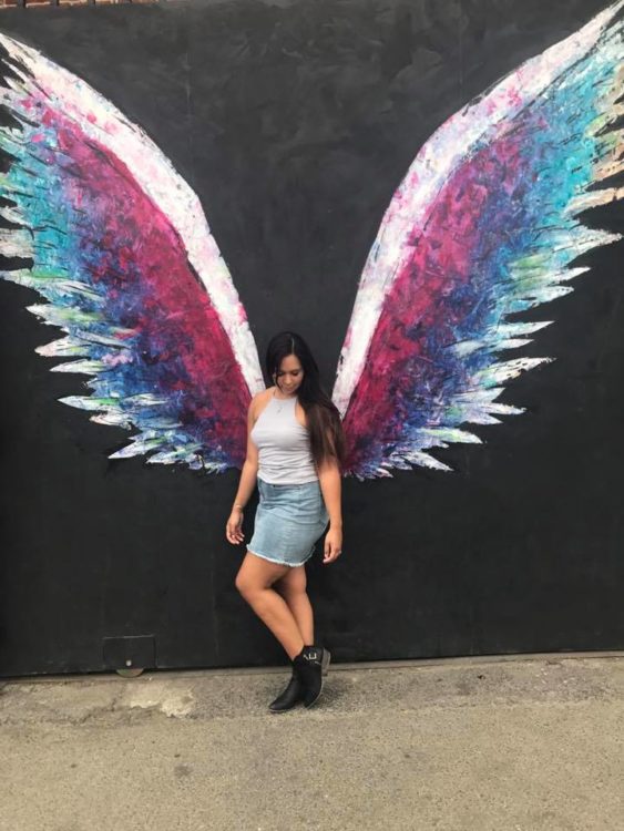 woman posing in front of angel wings graffiti